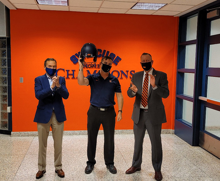 Charlie Poag holding up syracuse footbell helmet next to Mike Haynie and John Wildhack.