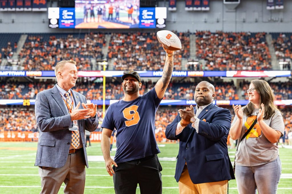 Varun as hometown hero holding a football in the dome. 