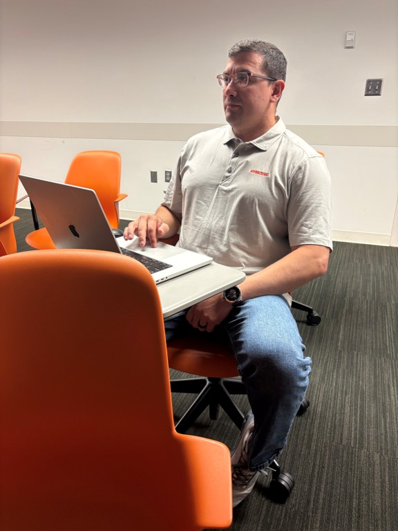 Joshua Carabajal in casual clothes working on laptop at SU.