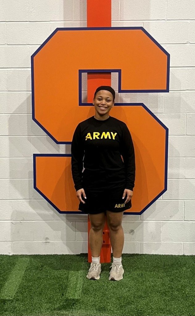 Mariah Carter in her PT gear standing in front of a giant S for SU.