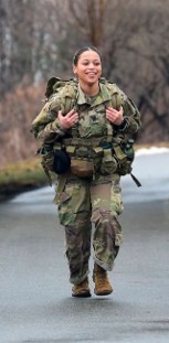 Mariah Carter in her full military gear doing a road march while smiling.